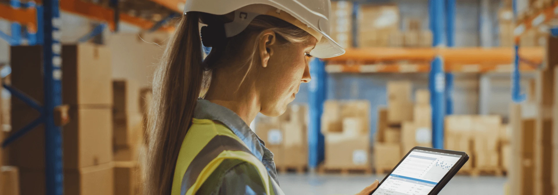 Warehouse worker in hard hat and safety vest checking inventory on a tablet
