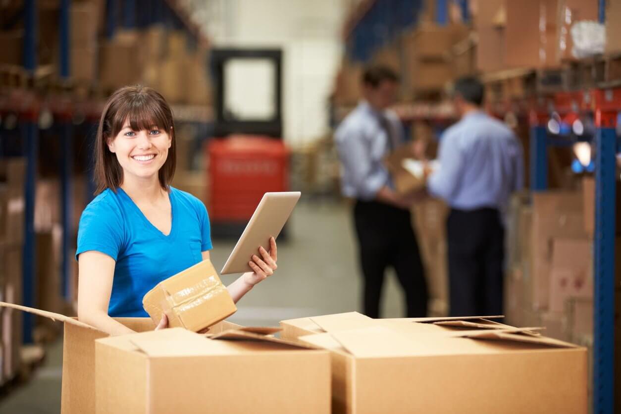 Smiling woman with tablet with boxes in a warehouse